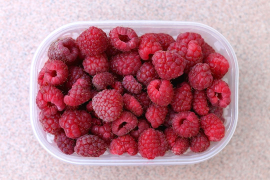 Fresh raspberries in a transparent plastic bowl. Top view, selective focus.