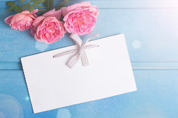 Pink  roses  and empty tag  on blue wooden background.