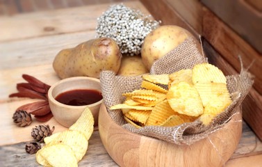 Potato chip and fresh potatoes on wood background