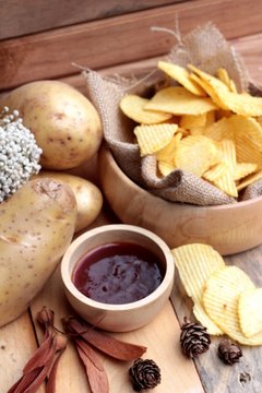 Potato chip and fresh potatoes on wood background