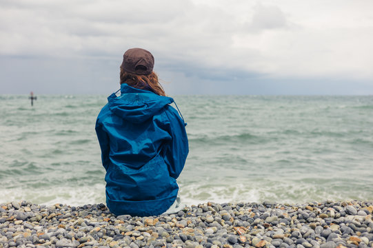Woman in blue jacket sitting on beach