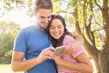 Fototapeta premium Cute couple using mobile phone in the park