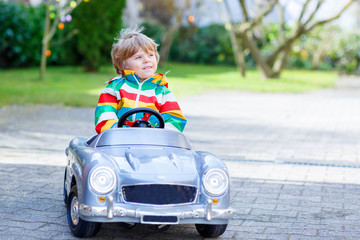 Little preschool boy driving big toy old vintage car, outdoors