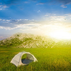 white touristic tent in a green hills at the sunrise