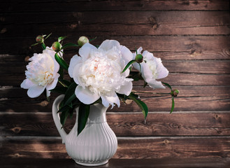 White peonies in a vase on a wooden background