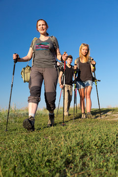 Family on vacation.
Group of three people of different age mother daughter son father walks consecutively along path on green grassy lawn blue sky on background
