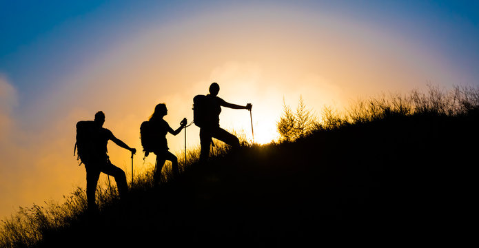 Climbers on grassy hill.
Family three people silhouette walking up steep grassy hill majestic sunrise and blue sky background