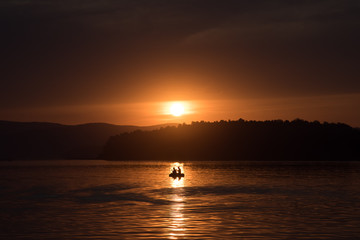 Silhouette of fisher and dog sitting in boat