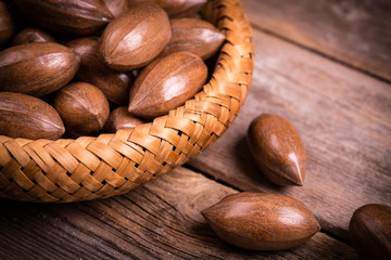 Whole pecan nuts in a wicker bowl, over vintage wood background.