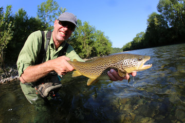 Closeup of fly-fisherman holding brown truit in river