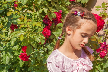 Portrait of  sad little girl against  background of rose bushes in  garden