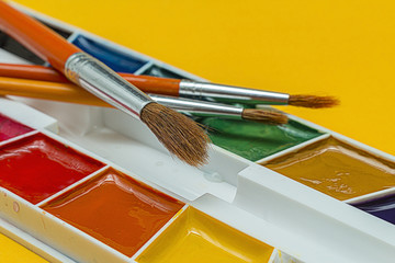 Brushes and watercolors on a yellow background