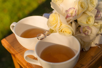 Wedding still life with two rings, cups of tea and bridal bouquet