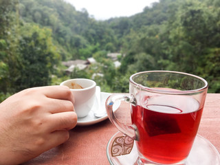 Hands holding coffee cups nearby tea glass with the mountain view
