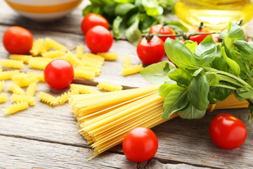 Spaghetti, basil and tomatoes on grey wooden background
