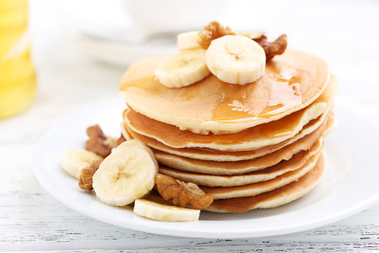 Tasty pancakes with banana and walnut on white wooden background
