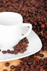 White cup with saucer on coffee beans