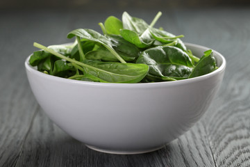 fresh spinach leaves in white bowl on wood table