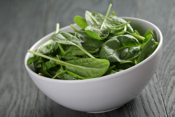 fresh spinach leaves in white bowl on wood table