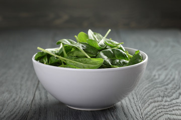 fresh spinach leaves in white bowl on wood table