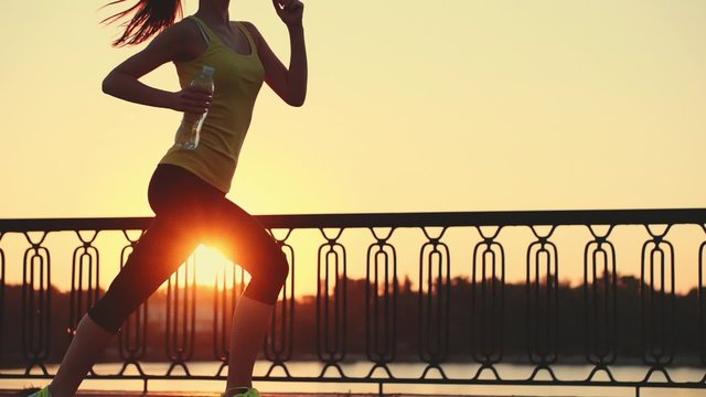 Slow motion: running woman. Runner is jogging in sunny bright light. Female fitness model training outside in the city on a quay. Sport lifestyle. Filmed at 240 fps.