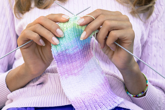 Woman knitting colorful scarf with her hands