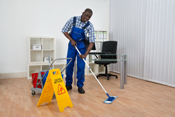 Fototapeta na wymiar Janitor Cleaning Floor With Wet Floor Sign