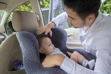 Father putting his baby on the car seat