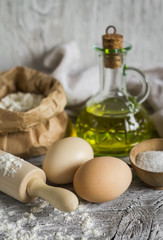 flour, olive oil, eggs - the ingredients to prepare the dough for pasta on a light wooden background