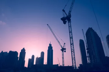Photo sur Plexiglas moyen-Orient Coucher de soleil sur les grues de construction parmi les gratte-ciel de tours de bureaux dans le centre commercial du Moyen-Orient, Dubaï
