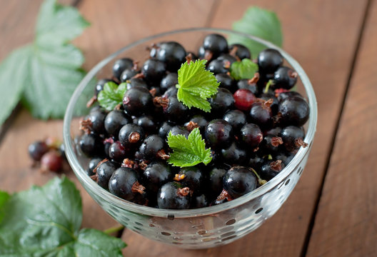Black currants in a glass bowl on a wooden background