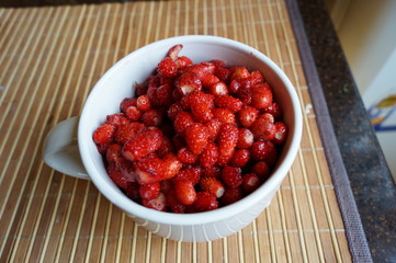 Red fresh wild strawberry in a big white mug stand on a table
