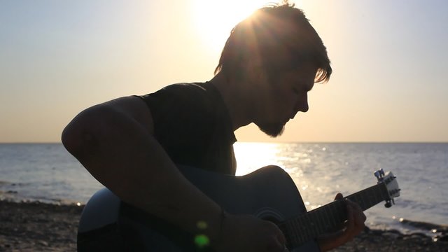 Silhouette of Bearded musician playing guitar in the beach