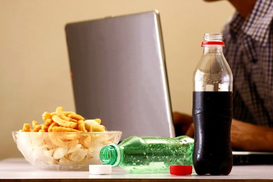 Bottles of softdrinks or soda, chips and man working on a laptop computer in the background