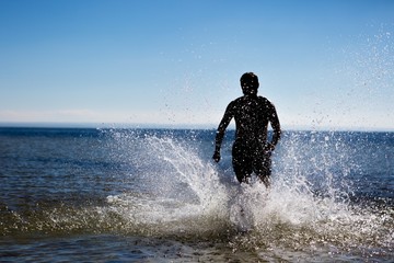 Man silhouette running through sea and splashing water.