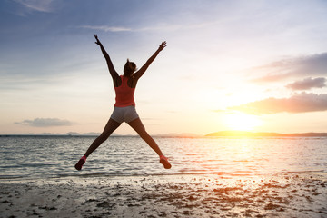Fototapeta na wymiar Sporty woman jumping on sunset at the beach.