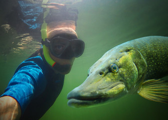 Underwater selfie with friend. Scuba diver and pike in deep lake.