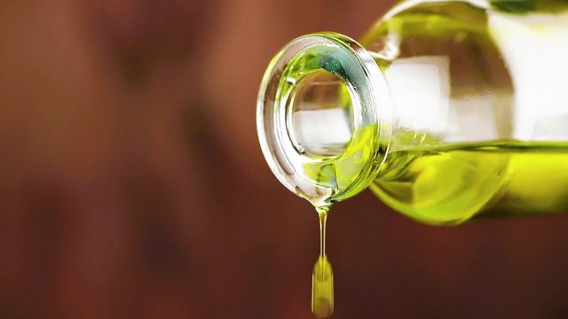 close-up of pouring olive oil with drops by bottle on wood background, concept of diet and nutrition 