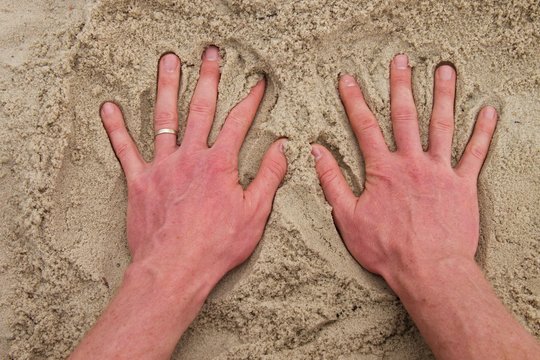 Male Caucasian hand in the salt sand on the beach.