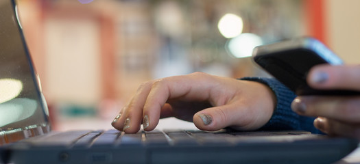 close up shot on hands over keyboard and laptop while connected with mobile phone - modern communications