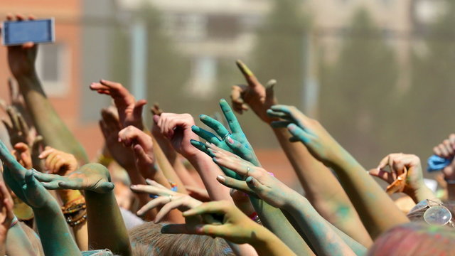 Crowd throwing hands up in air at Holi colors festival.
