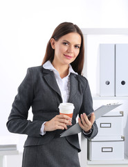 Attractive young businesswoman standing near desk with folder in