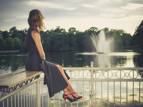 Elegant young woman sitting on jetty by pond in park
