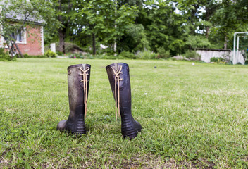 Two rubber boots on a green lawn near a red house in a farm
