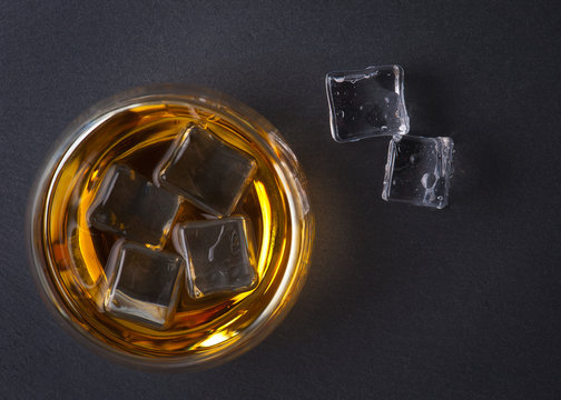 Glass of whiskey with ice on black stone table. Top view with copy space