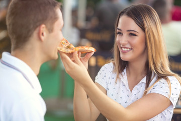 Beautiful young woman feeding her boyfriend with a slice of pizza