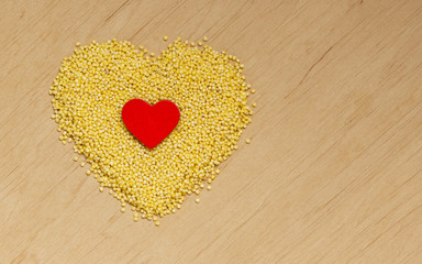 Millet groats heart shaped on wooden surface.