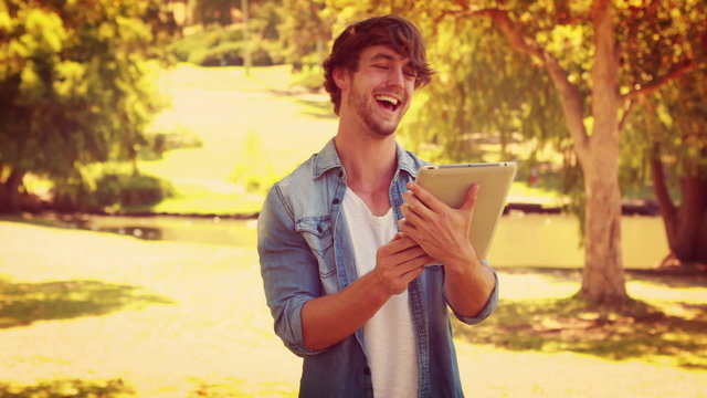 Handsome man using tablet and laughing in the park