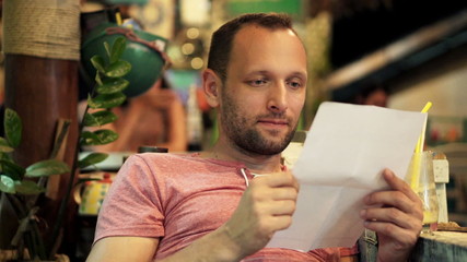 Happy, young man reading letter sitting in cafe
