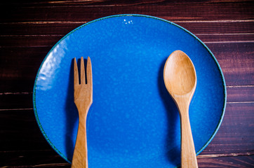 wooden spoon and fork in blue plate on wooden table background